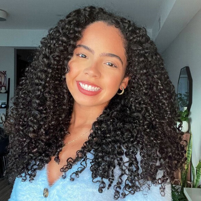 Model wearing a natural-black curly bob with a side part in indoor light.